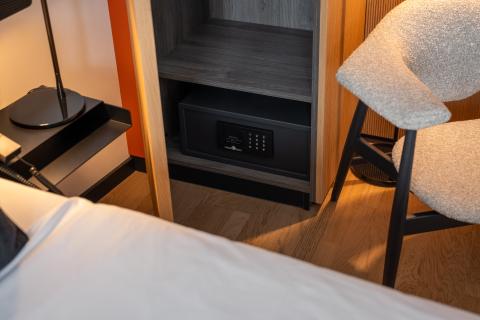 Corner of hotel bed with bedside table and comfortable armchair on the side