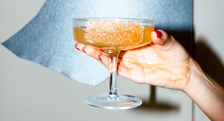 A hand with red painted nails is presenting an orange cocktail