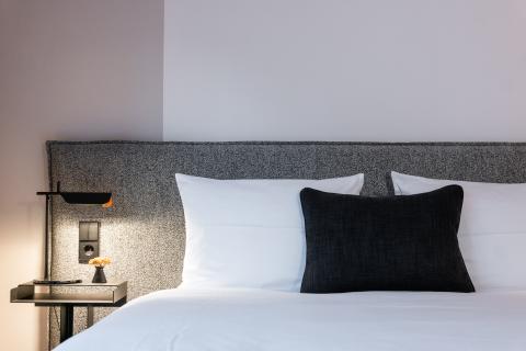 Doppelbett mit grauem Kopfende aus Stoff und einem Nachttisch mit Leselampe