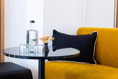 A yellow sofa with a marble table and two glasses next to a water bottle